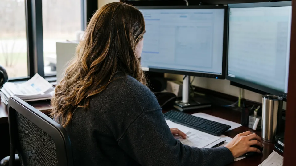 Treasury analyst uploading a batch of vendor wire payments to a corporate bank portal at a dual monitor desk